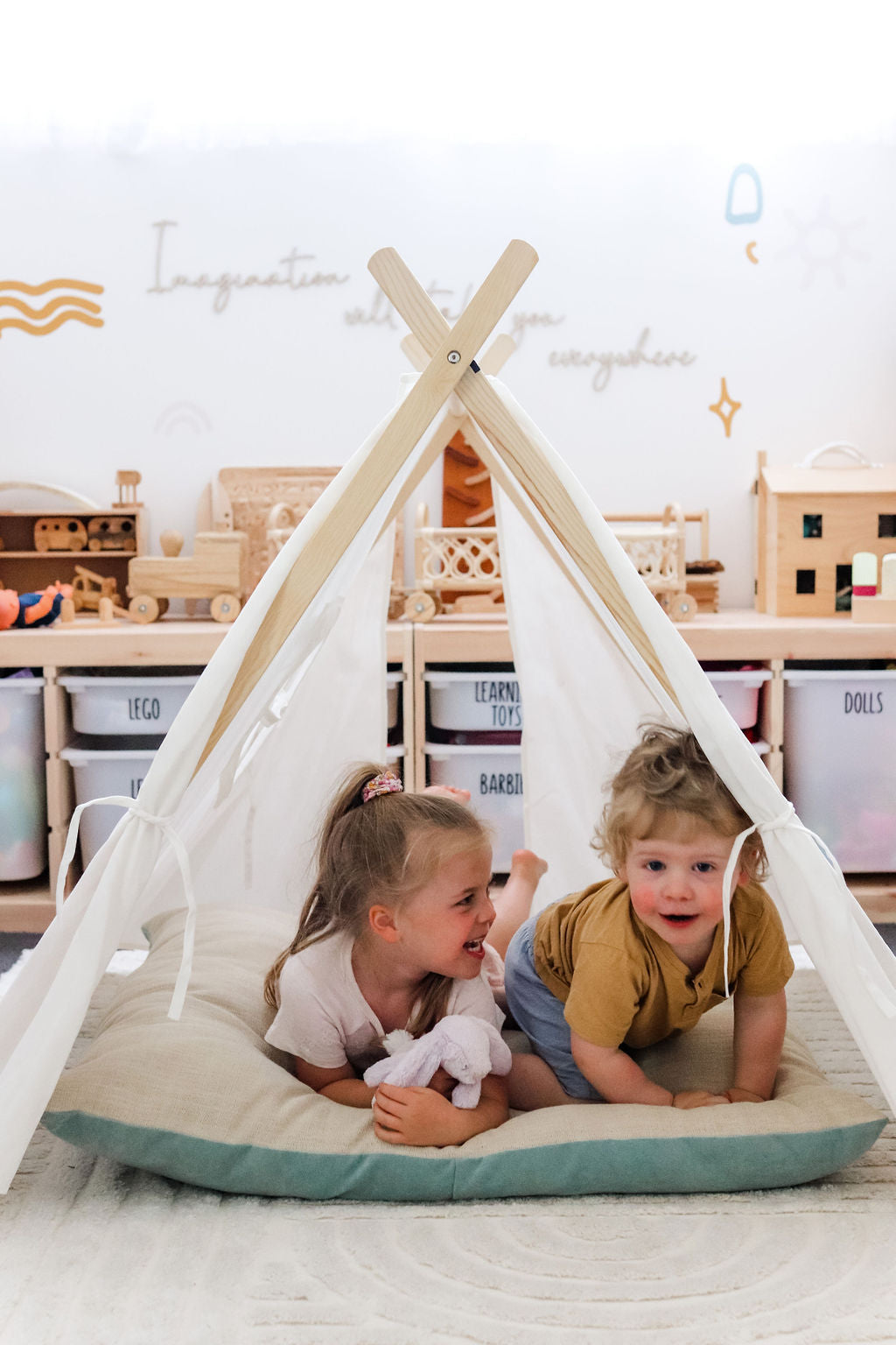 Image of 2 little children sitting below Petite Maison Play Safari Tent cubby on a floor cushion
