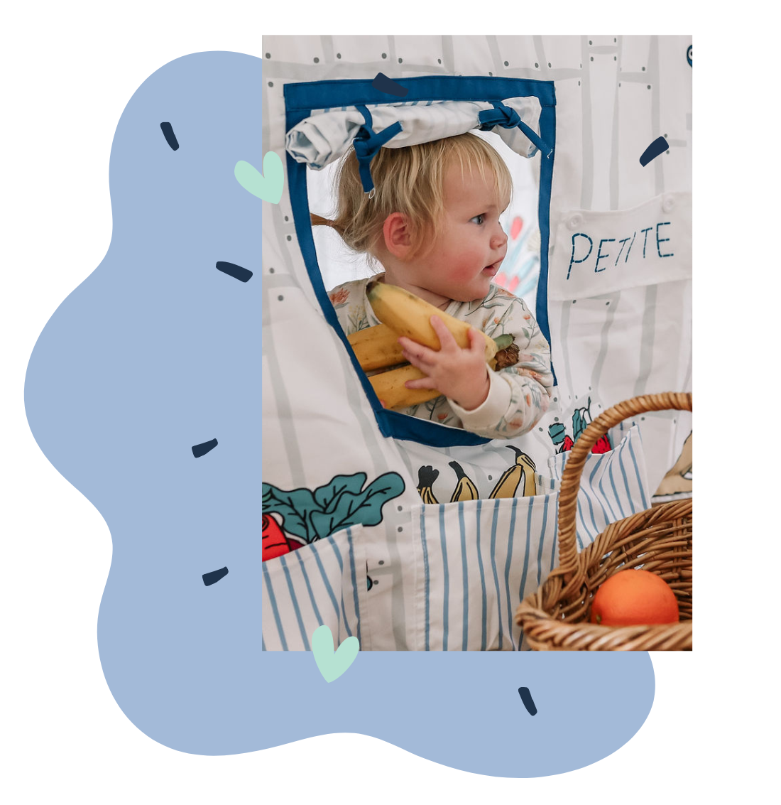 Image of child peeking out of Petite Maison Play Petite Shop Table Tent cubby holding a banana. 
