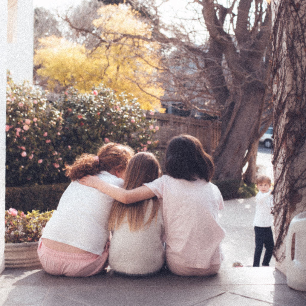 Three young children sitting together on porch over looking a garden where they can play in their cubby house